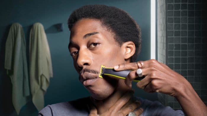 Man with smoldering expression trims moustache using the Philips OneBlade beard trimmer for men.