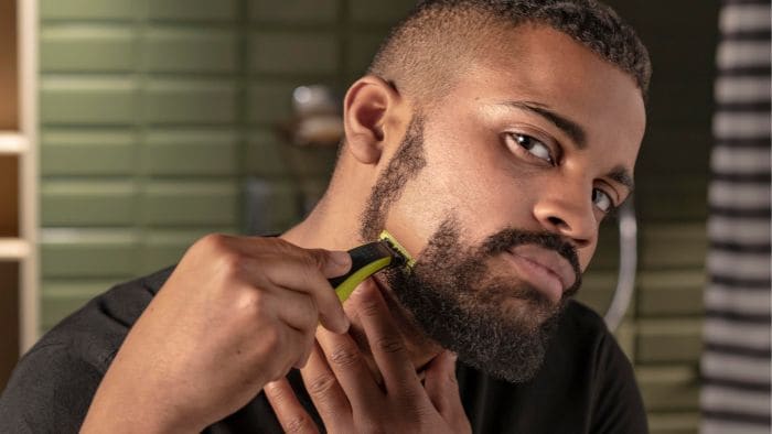 Man shaves cheek hair with the Philips OneBlade beard trimmer while looking in the mirror.