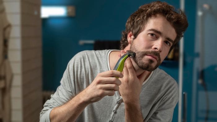 Man uses Philips OneBlade beard trimmer to shave neck hair while looking in the mirror.